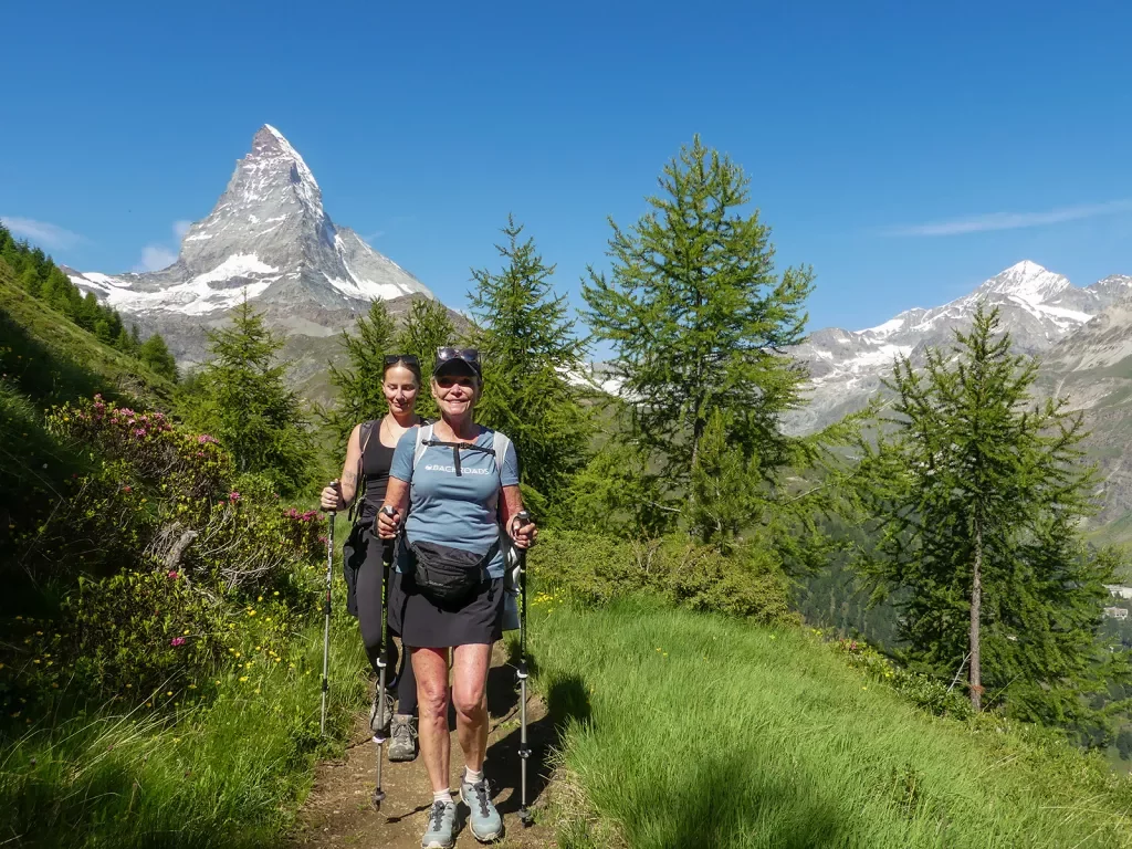 Two women with walking poles hiking on a grassy trail