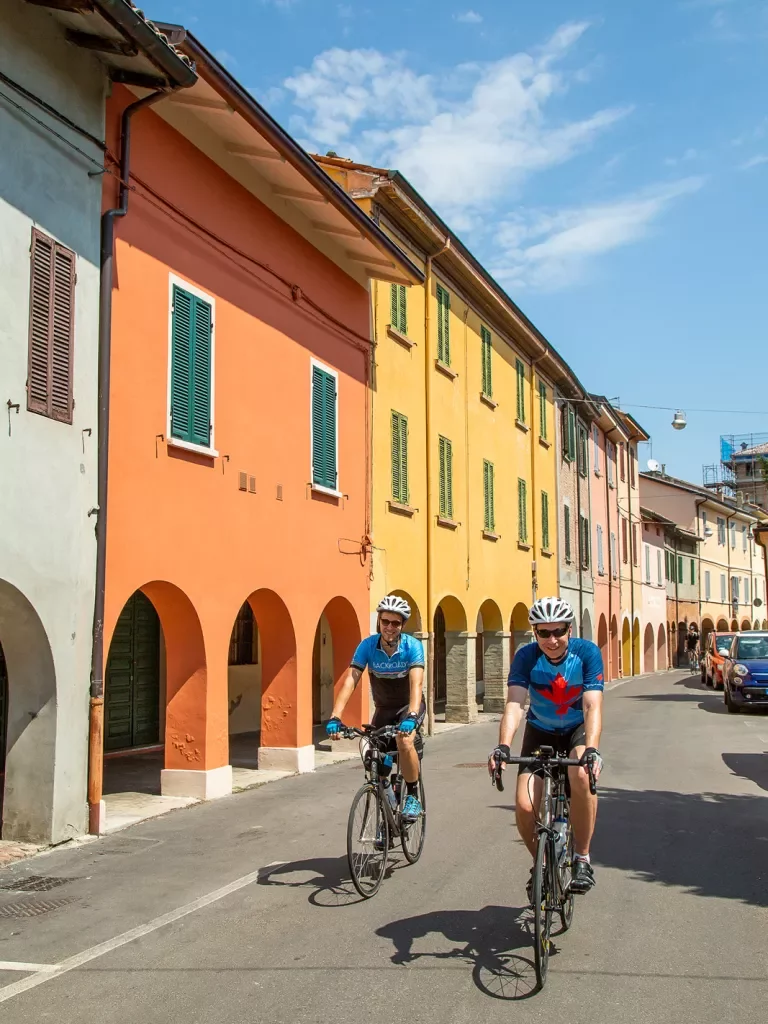Two bikers on a road next to colorful buildings