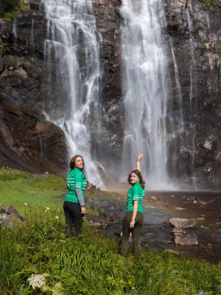 Two guests in bike jerseys pose with a waterfall